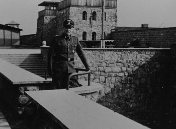 Movie still from “Night and Fog” (1956), directed by Alain Resnais – An old black and white photo of a man in a military uniform; Wide shot, High angle