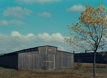 Movie still from “Night and Fog” (1956), directed by Alain Resnais – An old barn in the middle of a grassy field; Extreme Wide shot, Low angle