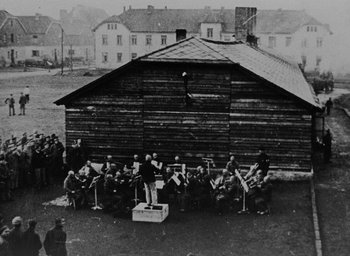 Movie still from “Night and Fog” (1956), directed by Alain Resnais – An old black and white photo of a group of people sitting in front of a building; Extreme Wide shot, High angle