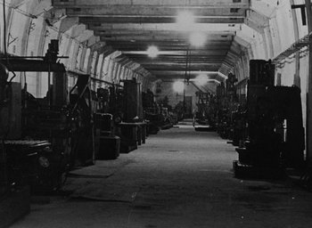 Movie still from “Night and Fog” (1956), directed by Alain Resnais – An industrial building with many machines inside of it; Extreme Wide shot, High angle
