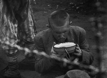 Movie still from “Night and Fog” (1956), directed by Alain Resnais – An old photo of a man holding a bowl in his hands; Medium shot, High angle