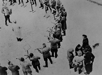 Movie still from “Night and Fog” (1956), directed by Alain Resnais – A group of men standing next to each other on snow; Extreme Wide shot, Over the shoulder angle