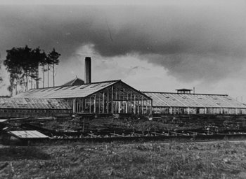 Movie still from “Night and Fog” (1956), directed by Alain Resnais – A black and white photo of a building in the middle of a field; Extreme Wide shot, Low angle
