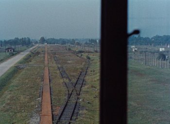 Movie still from “Night and Fog” (1956), directed by Alain Resnais – A view of an empty train track from a train window; Extreme Wide shot, High angle
