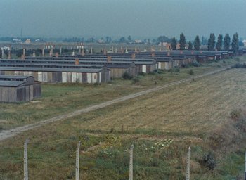 Movie still from “Night and Fog” (1956), directed by Alain Resnais – An old train yard with many buildings on it's side; Extreme Wide shot, High angle