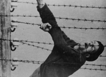 Movie still from “Night and Fog” (1956), directed by Alain Resnais – A man is holding his arms up in the air; Close Up shot, Low angle