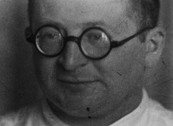 Movie still from “Night and Fog” (1956), directed by Alain Resnais – An old black and white photo of a man wearing glasses; Close Up shot, Low angle