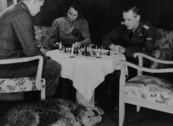 Movie still from “Night and Fog” (1956), directed by Alain Resnais – A black - and - white photo of a group of people sitting at a table; Wide shot, High angle