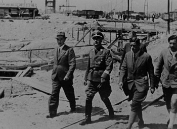 Movie still from “Night and Fog” (1956), directed by Alain Resnais – A group of men walking across a beach; Wide shot, Over the shoulder angle