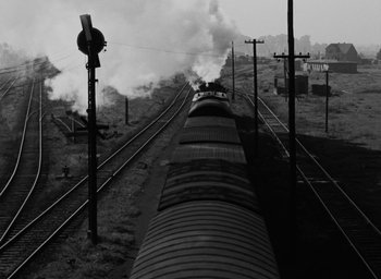 Movie still from “Night and Fog” (1956), directed by Alain Resnais – A black and white photo of a train going down the tracks; Extreme Wide shot, High angle