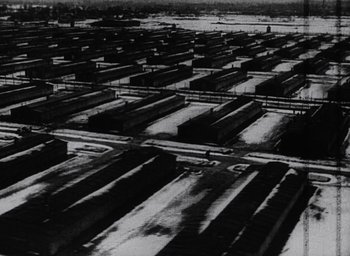 Movie still from “Night and Fog” (1956), directed by Alain Resnais – An aerial view of a train yard with many train cars; Extreme Wide shot, High angle