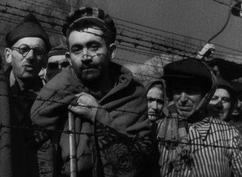 Movie still from “Night and Fog” (1956), directed by Alain Resnais – Black and white photograph of men behind barbed wire; Medium shot, Low angle