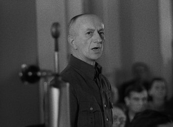 Movie still from “Night and Fog” (1956), directed by Alain Resnais – An older man in a military uniform speaking to an audience; Close Up shot, Over the shoulder angle