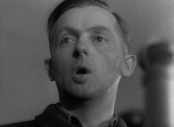 Movie still from “Night and Fog” (1956), directed by Alain Resnais – A black - and - white photo of a man with a surprised look on his face; Close Up shot, Low angle