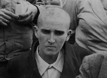 Movie still from “Night and Fog” (1956), directed by Alain Resnais – A black and white photo of a man with a shaved head; Close Up shot, High angle
