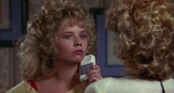 Movie still from “Night of the Comet” (1984), directed by Thom Eberhardt – A woman holding a cell phone in front of a mirror; Close Up shot, Over the shoulder angle