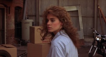 Movie still from “Night of the Comet” (1984), directed by Thom Eberhardt – A woman with long curly red hair standing in front of boxes; Close Up shot, Over the shoulder angle
