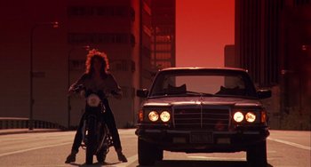 Movie still from “Night of the Comet” (1984), directed by Thom Eberhardt – A person on a motorcycle next to a parked car; Wide shot, Low angle