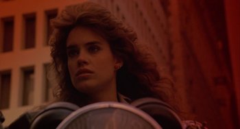 Movie still from “Night of the Comet” (1984), directed by Thom Eberhardt – A woman with long red hair standing in front of a building; Close Up shot, Low angle