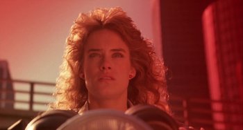 Movie still from “Night of the Comet” (1984), directed by Thom Eberhardt – A man with long blonde hair is looking at the camera; Close Up shot, Low angle