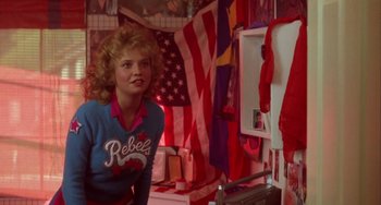Movie still from “Night of the Comet” (1984), directed by Thom Eberhardt – A young woman standing in front of an american flag; Medium shot, Over the shoulder angle