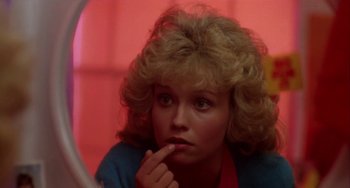 Movie still from “Night of the Comet” (1984), directed by Thom Eberhardt – A woman with blonde curly hair looking in a mirror; Close Up shot, Low angle