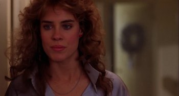 Movie still from “Night of the Comet” (1984), directed by Thom Eberhardt – A person with curly hair wearing a white shirt; Close Up shot, Over the shoulder angle