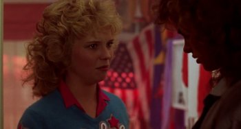 Movie still from “Night of the Comet” (1984), directed by Thom Eberhardt – A woman with blonde curly hair wearing a blue and red t - shirt; Close Up shot, Over the shoulder angle