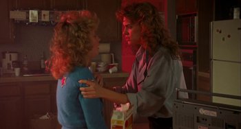 Movie still from “Night of the Comet” (1984), directed by Thom Eberhardt – Two women in a kitchen one is holding a box and the other is holding a drink; Medium shot, Over the shoulder angle