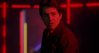 Movie still from “Night of the Comet” (1984), directed by Thom Eberhardt – A man in a black shirt is standing in a room; Close Up shot, Low angle
