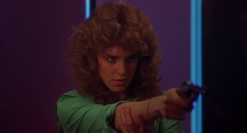 Movie still from “Night of the Comet” (1984), directed by Thom Eberhardt – A woman in a green shirt is holding a gun; Close Up shot, Low angle