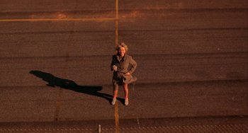 Movie still from “Night of the Comet” (1984), directed by Thom Eberhardt – A woman standing on the side of a road; Wide shot, Overhead angle