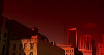 Movie still from “Night of the Comet” (1984), directed by Thom Eberhardt – A red sky with buildings in the background; Extreme Wide shot, Low angle