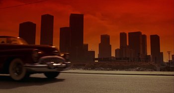 Movie still from “Night of the Comet” (1984), directed by Thom Eberhardt – A motorcycle riding down a street near a city; Extreme Wide shot, Low angle