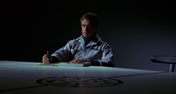 Movie still from “Night of the Comet” (1984), directed by Thom Eberhardt – A man sitting at a table writing on a piece of paper; Medium shot, Low angle