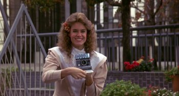 Movie still from “Night of the Comet” (1984), directed by Thom Eberhardt – A woman holding up a camera in front of a building; Close Up shot, Low angle