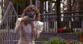 Movie still from “Night of the Comet” (1984), directed by Thom Eberhardt – A woman taking a picture with a camera outside; Medium shot, Over the shoulder angle