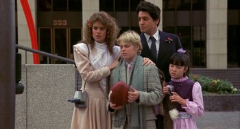 Movie still from “Night of the Comet” (1984), directed by Thom Eberhardt – A group of people standing next to each other holding a football; Medium shot, Over the shoulder angle