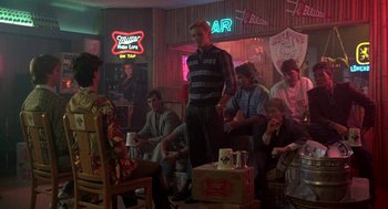 Movie still from “Night of the Creeps” (1986), directed by Fred Dekker – A group of people sitting in a room with neon signs; Wide shot, Over the shoulder angle