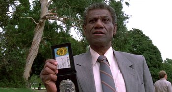 Movie still from “Night of the Creeps” (1986), directed by Fred Dekker – A man in a suit and tie holding a police badge; Close Up shot, Low angle