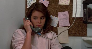 Movie still from “Night of the Creeps” (1986), directed by Fred Dekker – A woman holding a phone up to her ear while sitting in front of a bulletin board; Close Up shot, Low angle