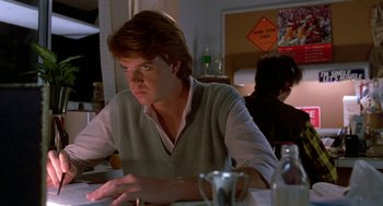 Movie still from “Night of the Creeps” (1986), directed by Fred Dekker – A man sitting at a table looking at a computer screen; Medium shot, Low angle