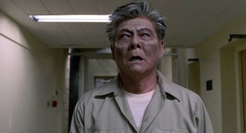 Movie still from “Night of the Creeps” (1986), directed by Fred Dekker – An older man with a gray hair and a gray shirt is looking at the camera; Close Up shot, Low angle