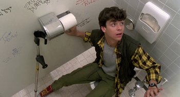 Movie still from “Night of the Creeps” (1986), directed by Fred Dekker – A young man sitting on the floor of a bathroom holding a roll of toilet paper; Medium shot, Low angle