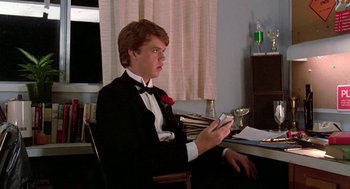 Movie still from “Night of the Creeps” (1986), directed by Fred Dekker – A man in a tuxedo sitting at a table with a cell phone in his hand; Medium shot, Low angle