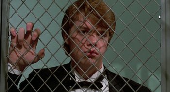 Movie still from “Night of the Creeps” (1986), directed by Fred Dekker – A man in a suit and bow tie behind a chain link fence; Close Up shot, Low angle