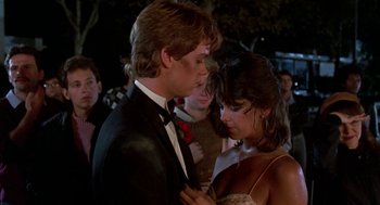 Movie still from “Night of the Creeps” (1986), directed by Fred Dekker – A man and a woman in formal wear standing next to each other in a crowd; Medium shot, Over the shoulder angle