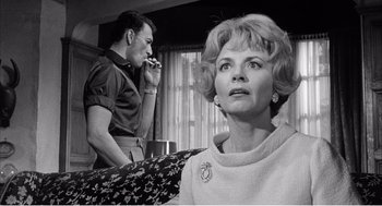 Movie still from “Night of the Eagle” (1962), directed by Sidney Hayers – An older woman smoking a cigarette in front of a younger man; Close Up shot, Low angle
