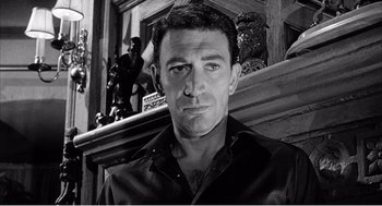 Movie still from “Night of the Eagle” (1962), directed by Sidney Hayers – Black and white photograph of a man in front of a fireplace; Close Up shot, Low angle