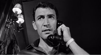 Movie still from “Night of the Eagle” (1962), directed by Sidney Hayers – A black and white photo of a man holding a phone to his ear; Close Up shot, Low angle